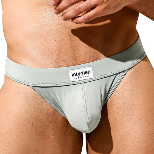 A close-up highlights the Intymen Obscene Bikini, focusing on its light gray hue, waistband, and fabric texture. Its high-cut design provides a stylish yet snug fit for comfort.