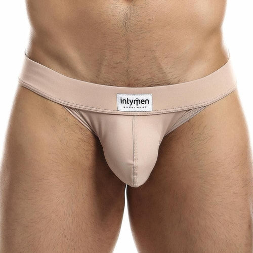 A close-up image features someone in light beige Intymen Obscene Bikini underwear. The smooth fabric ensures comfort and highlights the high-cut design, with the Intymen brand label visible on the waistband, all set against a plain white background.