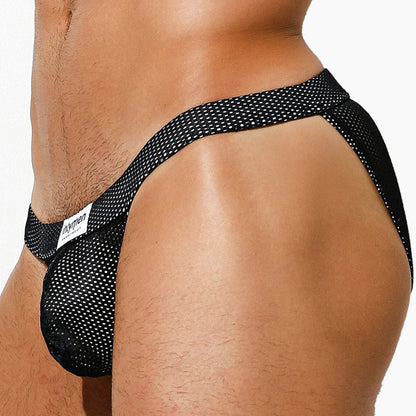 A close-up side view shows someone in Intymen Palatino Bikini Underwear, showcasing a black mesh jockstrap with a sheer pouch and a small white logo tag on the waistband. The plain white background accentuates the design and texture of the garment.