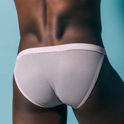 A person wears Intymen Palatino Bikini in light pink mesh, highlighting its breathable design against a blue background with the sheer fabric pouch accentuating the lower back and hips.