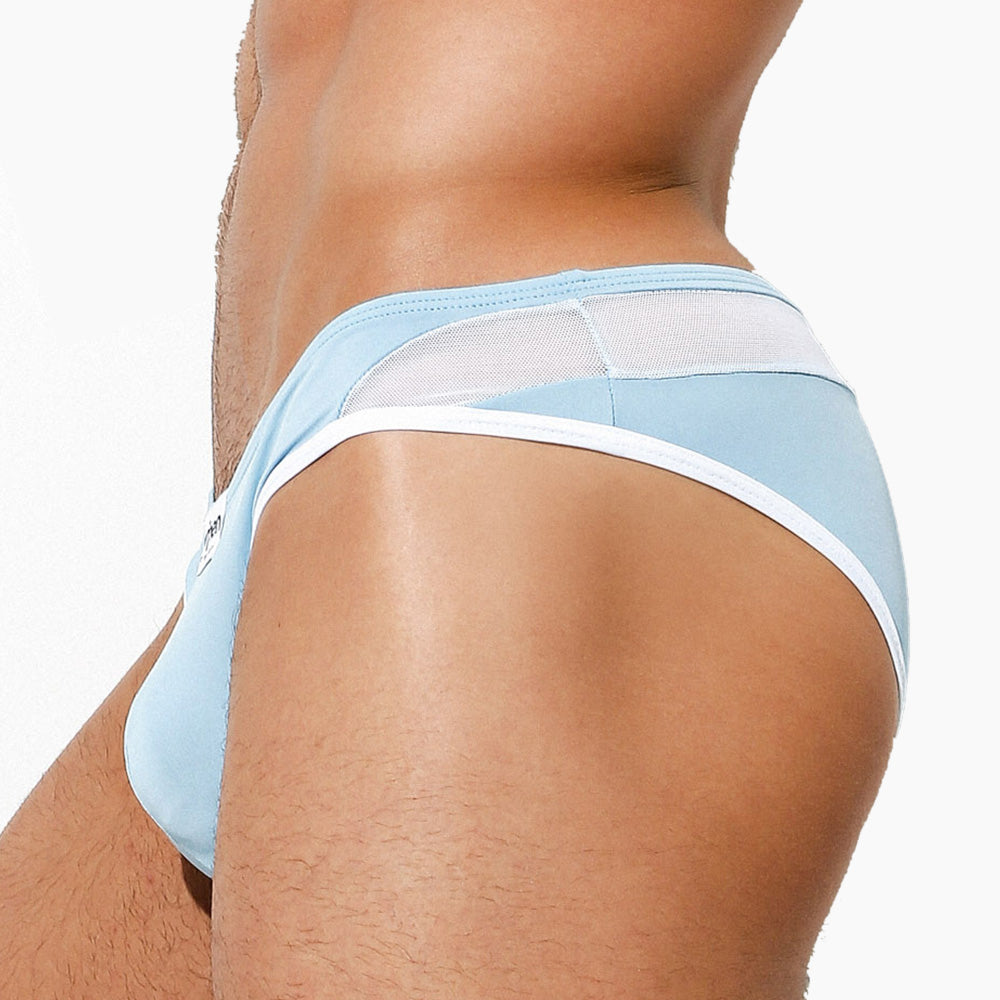 A person is seen in a close-up, sporting light blue and white Intymen Veneto Bikini briefs made from breathable polyamide and spandex, facing sideways.