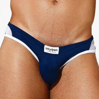 A person is wearing Intymen Veneto Bikini in dark blue and white, showcasing the front design, label, and sheer texture of the breathable polyamide-spandex blend fabric.