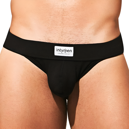 The image shows a person wearing black Intymen Fresh Bikini briefs with Intymen on the waistband, crafted from a premium fabric blend. The focus is on the midsection to highlight the design and fit of this bikini-style underwear.