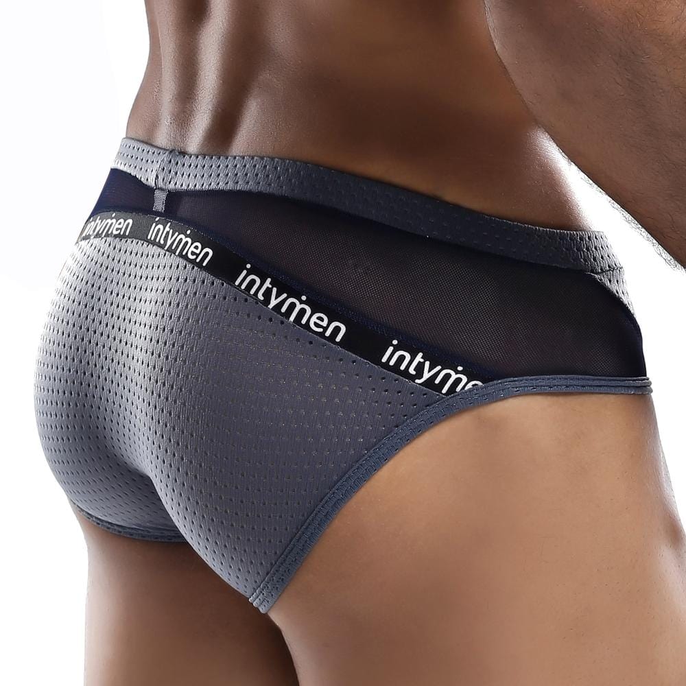 A person models Intymen Serenity Briefs, featuring black mesh details and a waistband branded with Intymen. The focus is on the back view, showcasing the sheer fabric design and texture.