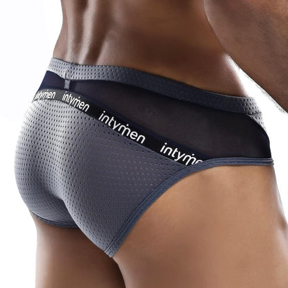 A person models Intymen Serenity Briefs, featuring black mesh details and a waistband branded with Intymen. The focus is on the back view, showcasing the sheer fabric design and texture.