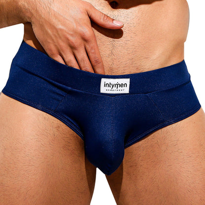 Someone wearing dark blue Intymen Femme Briefs with a visible Intymen waistband label. The focus is on the lower torso, highlighting the style and comfort of these briefs against a light background.