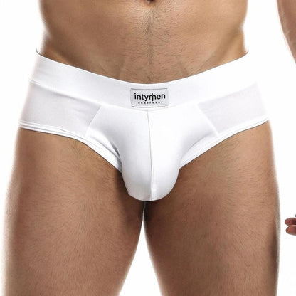 A person wearing sleek white Intymen Femme Briefs stands against a plain backdrop, showcasing the stylish waistband that displays Intymen, emphasizing comfort and fashion in this focused shot of the lower torso and underwear.