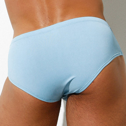 A person is seen from the back wearing Intymen Amore Brief, highlighting light blue mens briefs with contoured pouch support by Intymen, crafted from luxurious fabric against a neutral background.