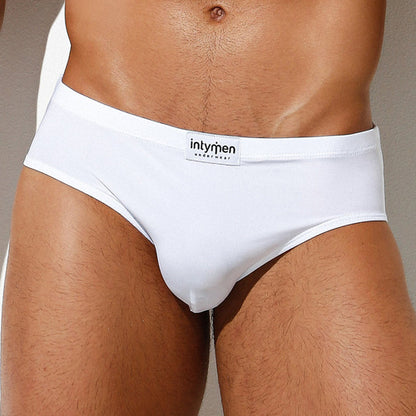 A person wears the white Intymen Amore Brief, showcasing a visible waistband label, luxurious fabric, and contoured pouch support against a neutral background.