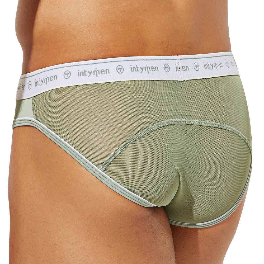 A person is seen in green Intymen See Through Back Briefs, featuring a white waistband with the brand name Intymen. The image highlights its see-through back and breathable cotton fabric, merging comfort with style from side and back views.