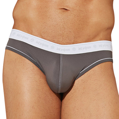 A person models Intymen See Through Back Briefs in gray, made from breathable cotton with a white waistband featuring circular logos and intymen text. The briefs include white trim, and the image shows their torso from the waist down.