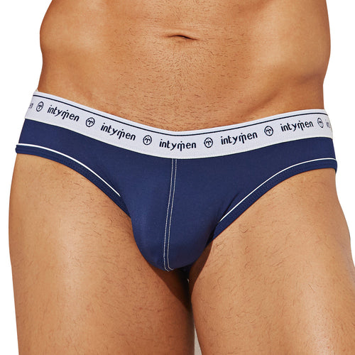 A person is wearing Intymen See Through Back Briefs in navy blue with a white waistband featuring Intymen in black. The breathable cotton fabric ensures comfort, and the sides have stylish white piping.