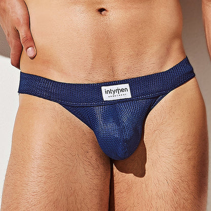 A person wears the Intymen Mesh Seductive Thong, featuring a blue breathable mesh waistband with a white intymen label in black text. The fabric has a textured look that accentuates its V-shape design against a neutral wall backdrop.