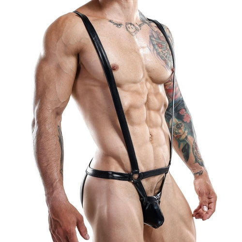 A muscular individual, intricately tattooed, wears the Miami Jock Bodysuit from Miami Jock—a black leather harness with a bold jockstrap design—highlighting their physique. They pose against a plain white background, head not visible.