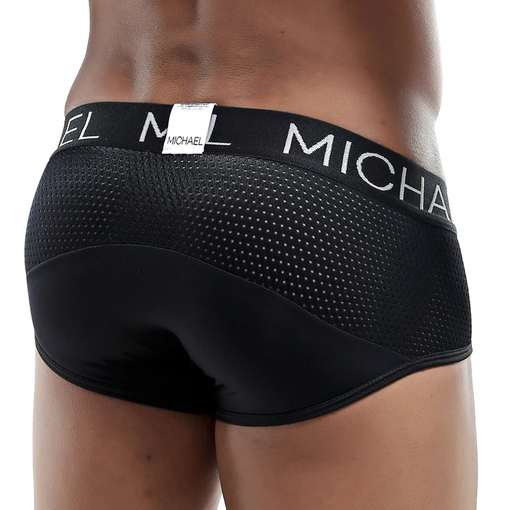 A person wearing Michael Brief black mesh underwear from behind showcases a sleek, defining fit that offers style, comfort, and support, with the waistband displaying Michael in white letters.