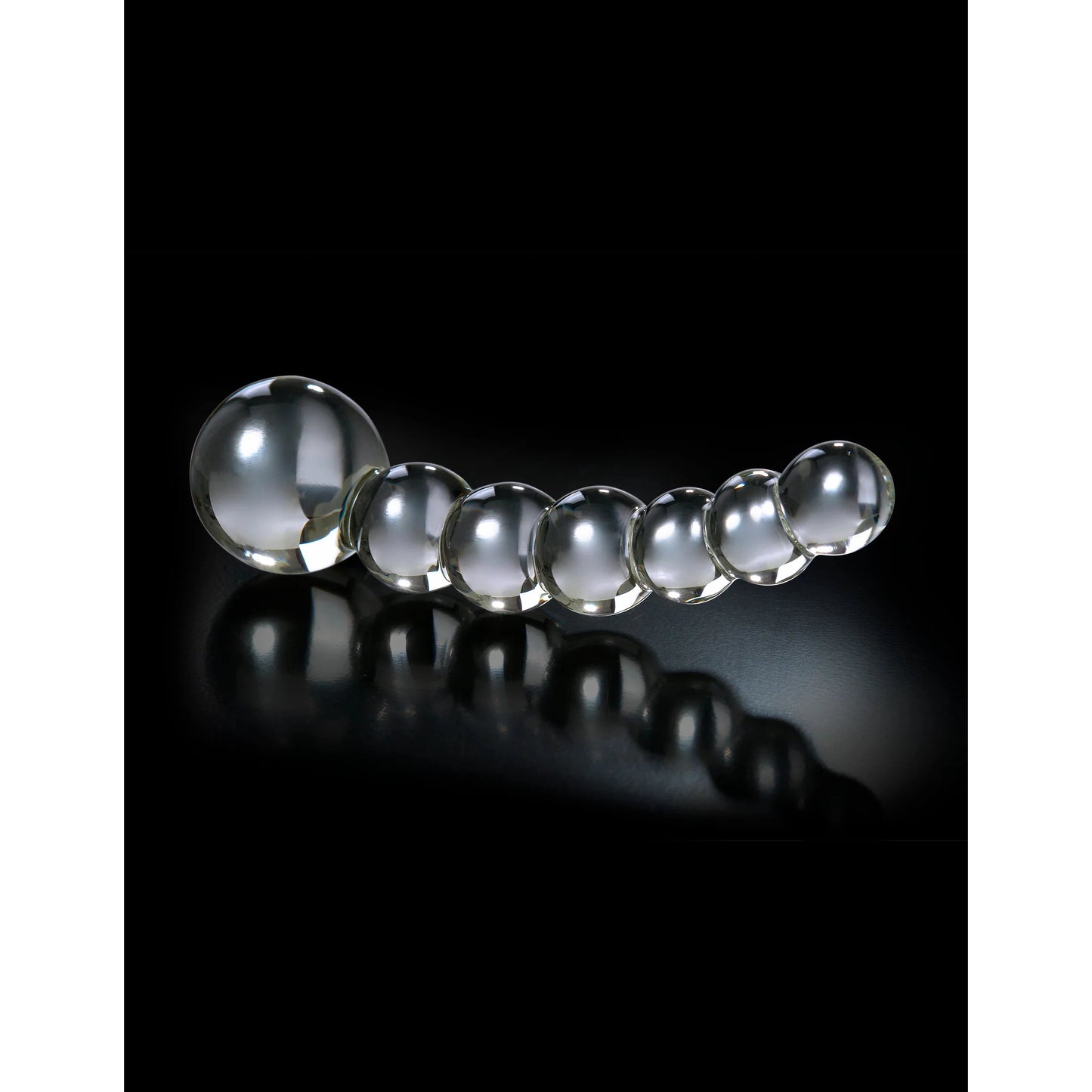 A series of seven Icicles No. 66 Hand Blown Glass Dong spheres by Pipedream are elegantly lined on a black reflective surface, decreasing in size from left to right with the largest sphere prominently on the left.