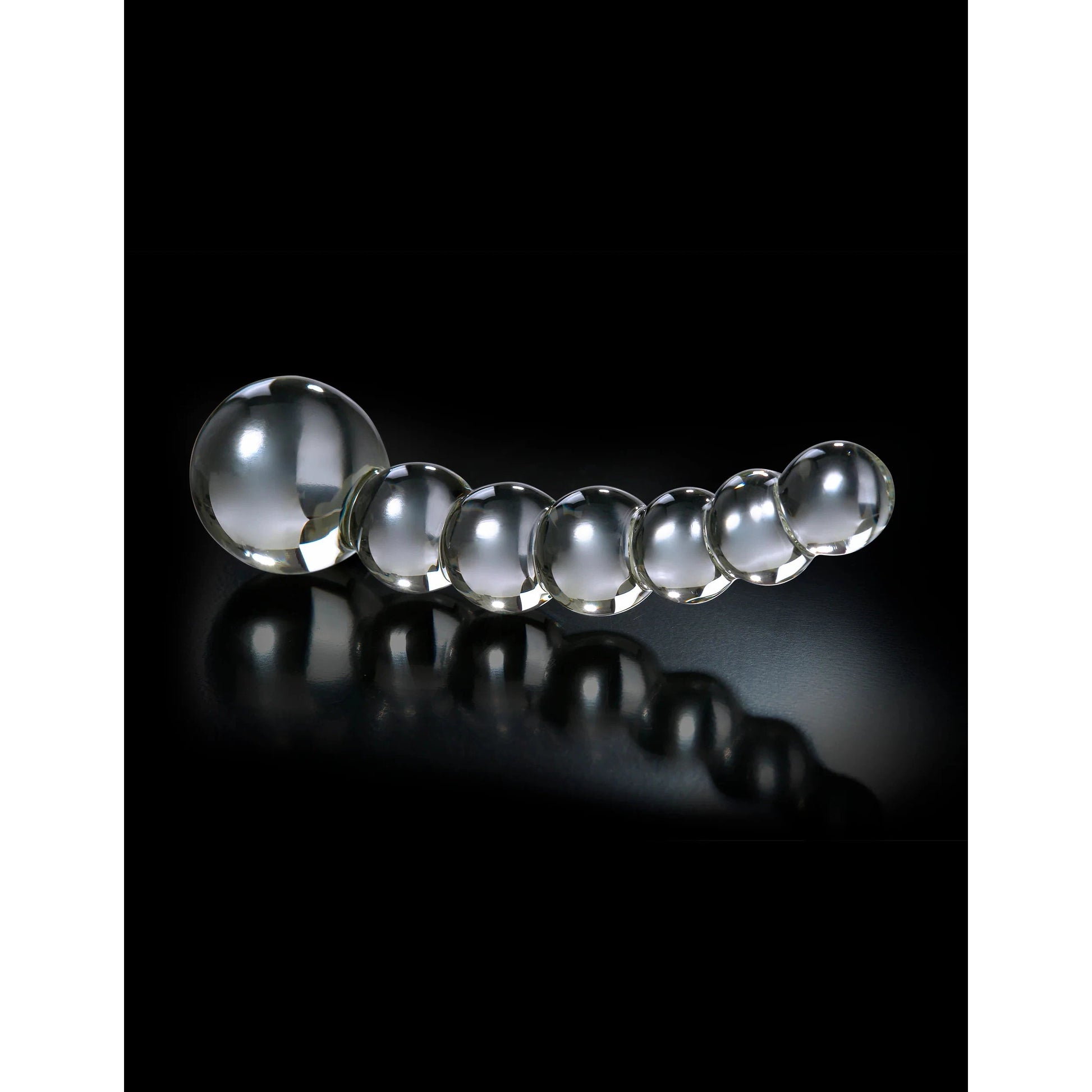 A series of seven Icicles No. 66 Hand Blown Glass Dong spheres by Pipedream are elegantly lined on a black reflective surface, decreasing in size from left to right with the largest sphere prominently on the left.