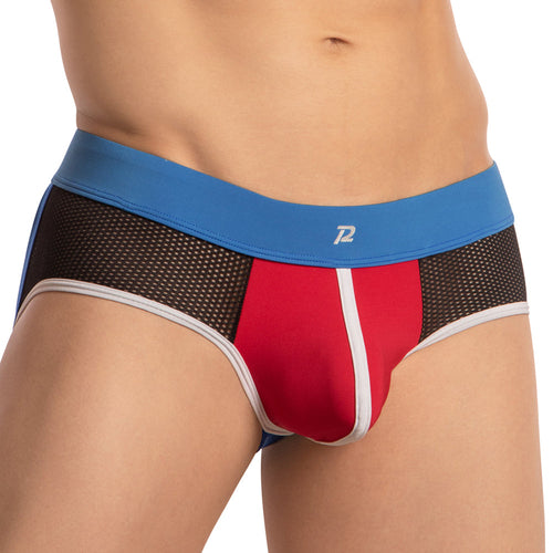 A person is wearing Pistol Petes Piping Bulge Pouch Jockstrap, featuring a multicolored design with a blue waistband, red front panel, black side net fabric, white trim, and a small logo on the waistband. The torso is visible while the head remains unseen.