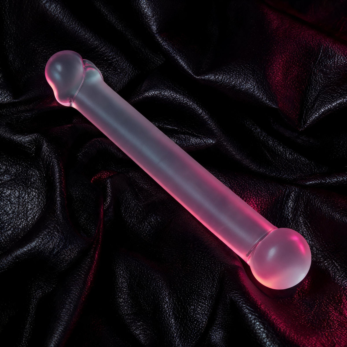 The Gläs 7" Realistic Head Glass Dildo by Gläs, featuring a translucent hand-blown design and rounded tip, glows softly pink on a textured black leather surface under dramatic red and purple lighting.