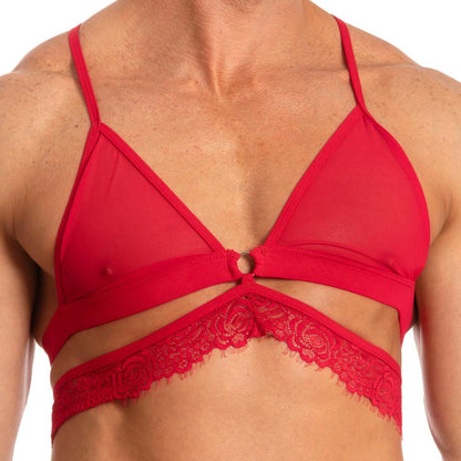 Someone is wearing the Secret Male SMA017 Justines Delight Bra, a red lace bralette with thin straps, floral detailing made from polyamide, featuring a central ring and lace band, shown against a plain white background.