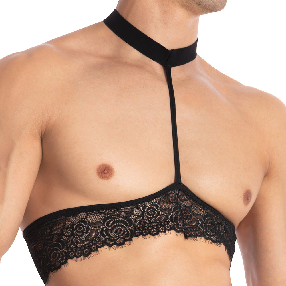 A person confidently wears the Secret Male Throbbin Top, a black halter neckline bralette with floral lace detailing and a collar strap, showcasing bold mens fashion against a white background.