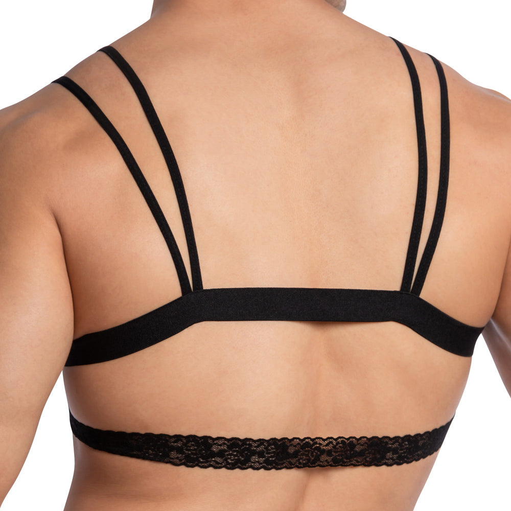 The image showcases a person wearing Secret Males Catrina Sexy Top, a black strappy bralette with lace trim. The focus is on the back, highlighting the unique strap design and delicate lace detail along the bottom, embodying a blend of style and sophistication.