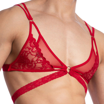 A person wearing the Secret Male Catrina Sexy Top, a red lace harness with triangular cups, ring details, and multiple chest straps. The sheer fabric with lace accents mirrors the intricate style of this top by Secret Male.