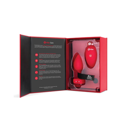 The open box reveals sleek, modern packaging in black and red, displaying a b-Vibe Vibrating Heart Plug adult toy set. On the left are a remote control and clear instructions for your anal adventures, featuring the b-vibe plug for added excitement.