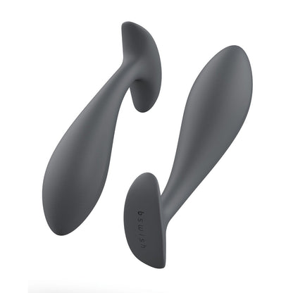 Two Bfilled Basic Plug prostate massagers in sleek, dark gray are showcased from various angles. Each features a curved, ergonomic design with a flared base for safety and a tapered head for increased anal pleasure. The soft silicone texture is highlighted by one being horizontal and the other vertical.