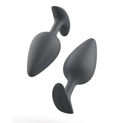 Against a white backdrop, two grey silicone Bfilled Basic Plus butt plugs by Bfilled are shown. They are waterproof and tapered with flared bases, available in different sizes for comfortable anal play.