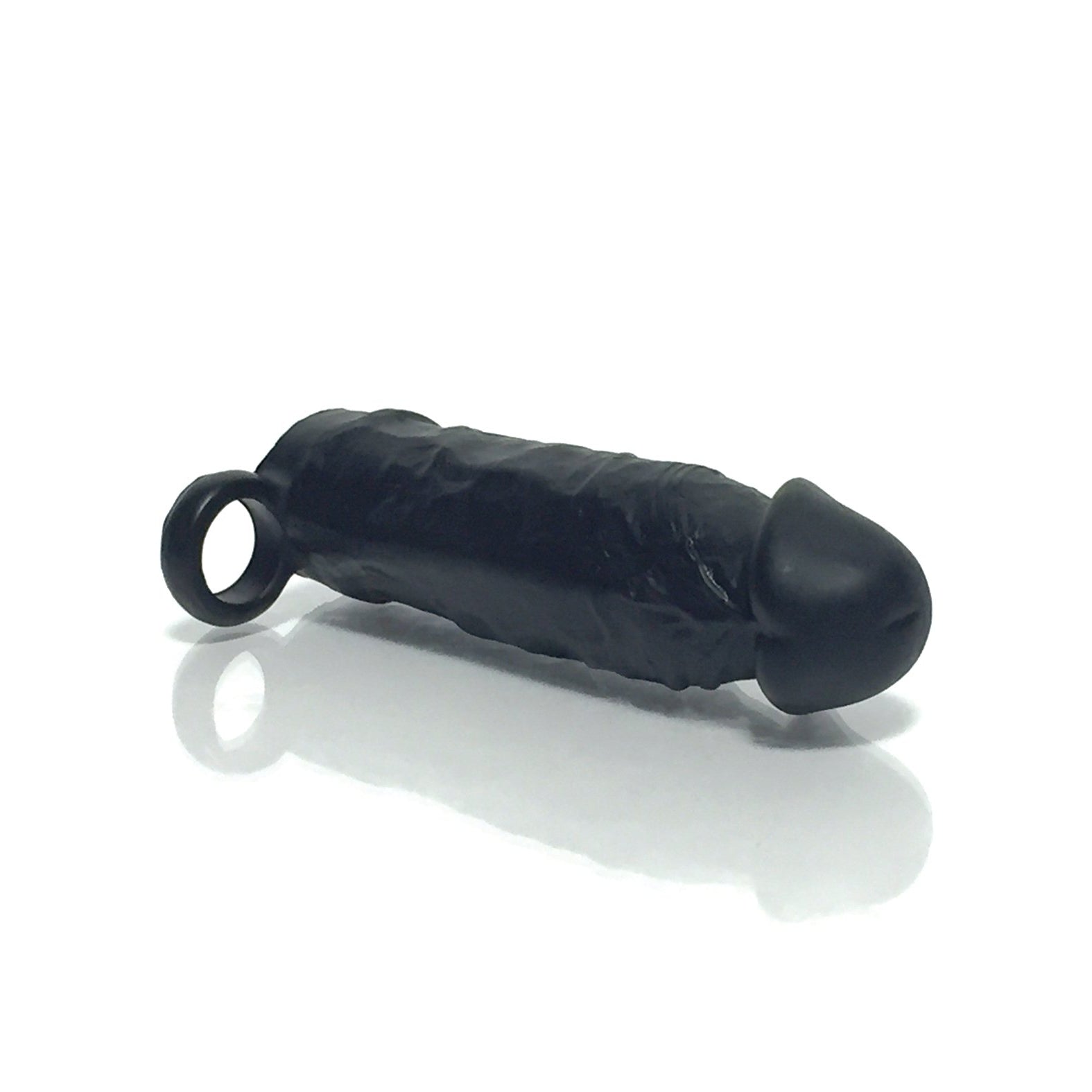 The Boneyard The Man Sizer 3X Stretch Silicone Extender by Boneyard is a black, cylindrical silicone device with a rounded tip and loop at the end, resembling a sleek sleeve, elegantly resting on a reflective white surface.