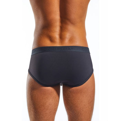 The image shows a tan male model wearing Cocksox Contour Pouch Sports Black Briefs. Made from Supplex fabric, the briefs have a waistband with OCKSOX partially visible. The background is plain and bright.