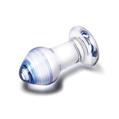 The Gläs Pleasure Droplets Anal Training Kit features a transparent, smooth glass butt plug with a flared base and rounded, tapered tip. Its design showcases swirling blue hues along the body set against a white background.
