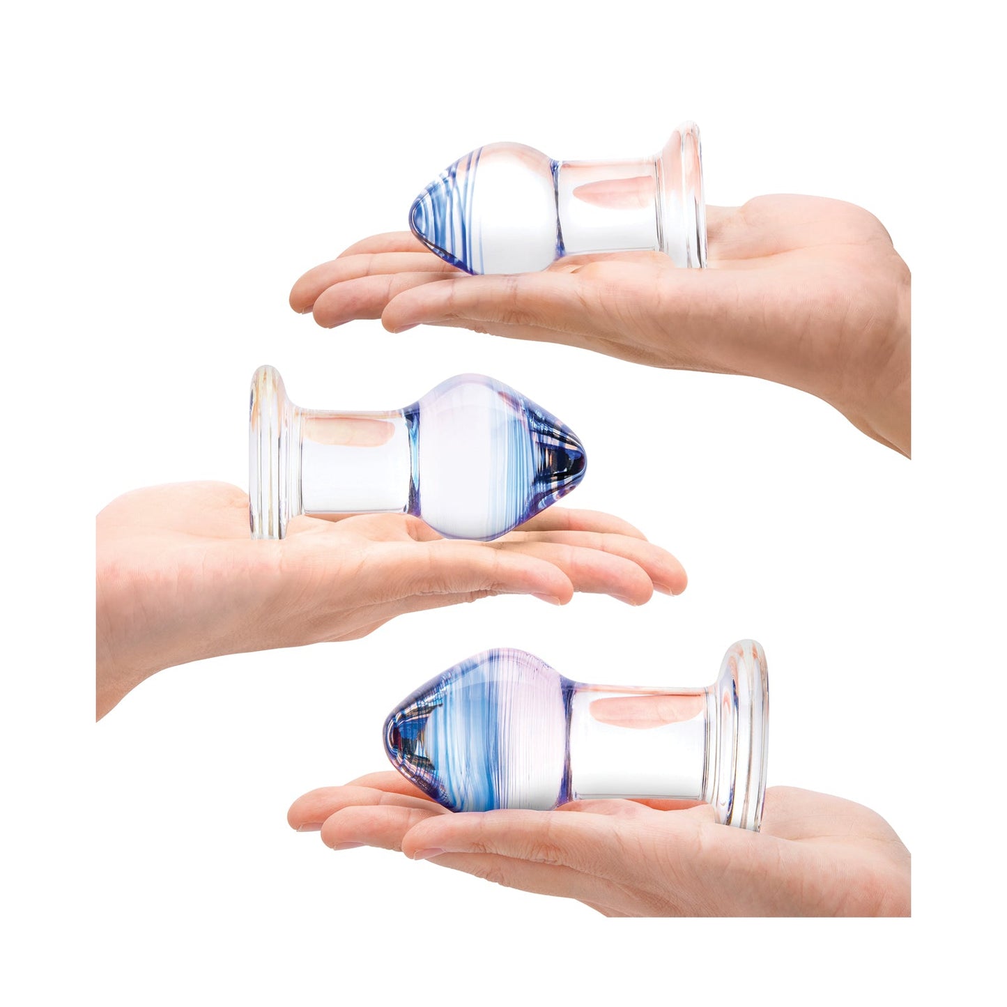 Three hands hold transparent glass objects from the Gläs Pleasure Droplets Anal Training Kit, resembling a bulbous tip and flat base. The pieces vary slightly in size and colors, featuring blue and purple hues, all set against a plain white background.