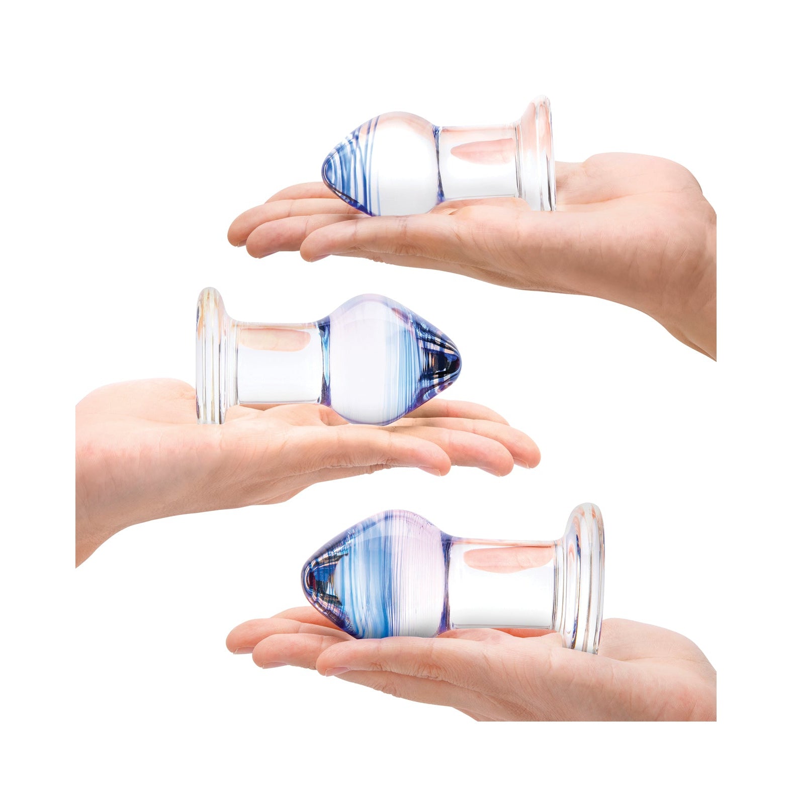 Three hands hold transparent glass objects from the Gläs Pleasure Droplets Anal Training Kit, resembling a bulbous tip and flat base. The pieces vary slightly in size and colors, featuring blue and purple hues, all set against a plain white background.