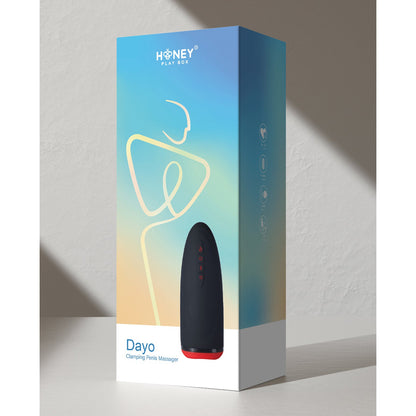 A product box labeled Honey Play Box features a black device with red accents on a gradient backdrop, showcasing the Dayo Autoblowjob Clamping Penis Massager and highlighting its automatic clamping technology for an enhanced experience.