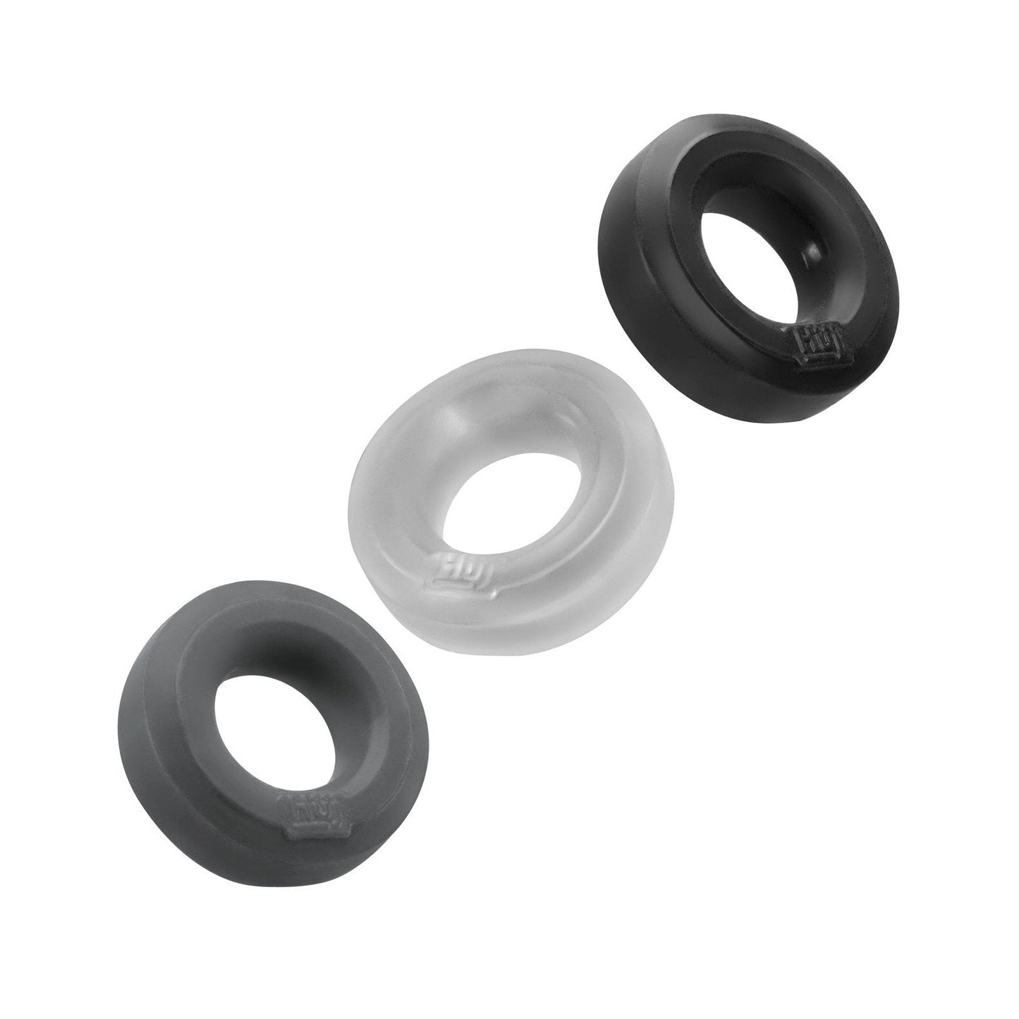 The Hunky Junk C Ring Multi Pack includes three rings in dark gray, transparent, and black. They are diagonally aligned against a white backdrop, boasting smooth surfaces and subtle branding.
