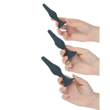 Three hands showcase the Lux Active Equip Silicone Anal Training Kit from LUX, featuring dark green silicone plugs of varying sizes with a smooth, tapered design perfect for easy application of lubricant against a white background.