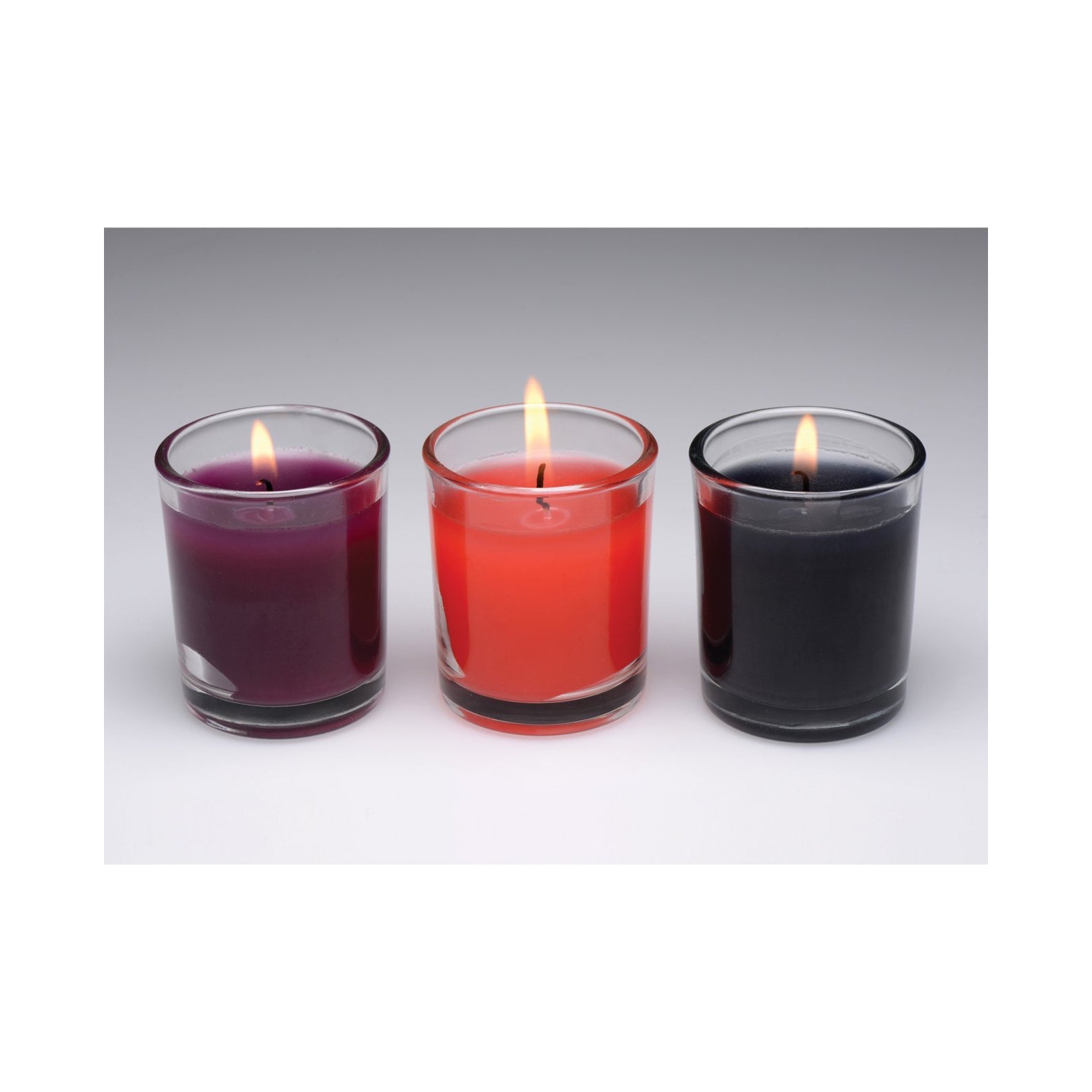 The Master Series Flame Drippers Candle Set features three BDSM candles in glass holders, showcased against a plain background. From left to right, the colors are purple, red, and black.