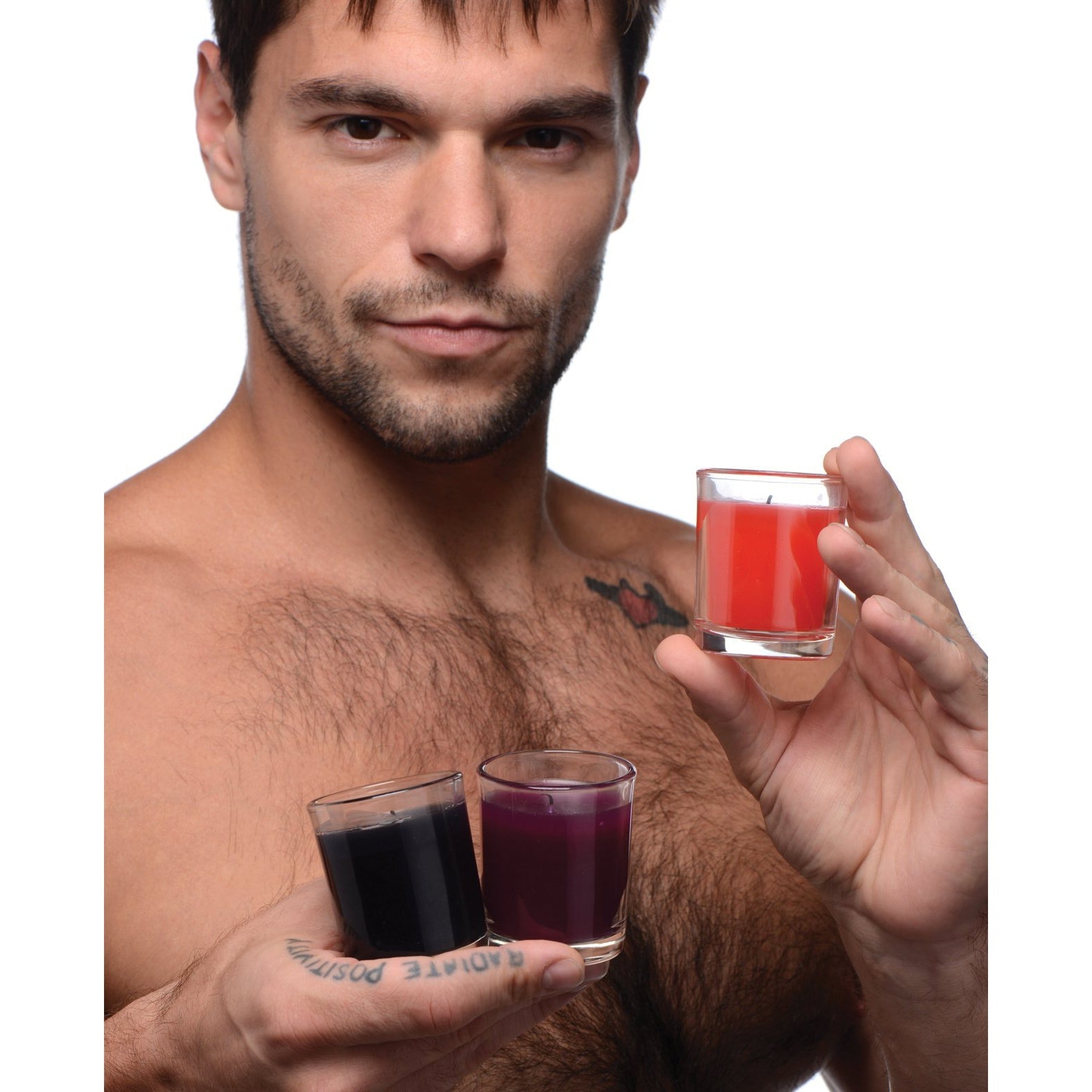 A shirtless man with a tattoo on his hand holds three Master Series Flame Drippers BDSM candles in red, purple, and black glass containers against a plain white background. Perfect for candle play.