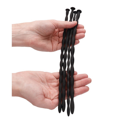 Two hands hold the Adams Toy Box Shots Ouch Advanced Urethral Sounding Silicone Spiral Plug Set, featuring three flexible black wavy rods with rounded ends against a plain white background.