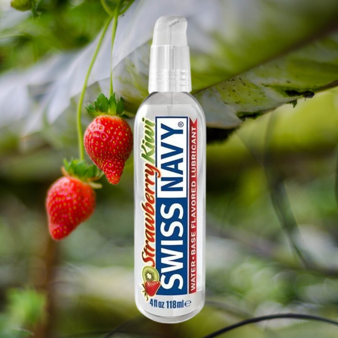 A 4 fl oz Swiss Navy Flavors bottle with strawberry kiwi flavors and a non-sticky formula is pictured outdoors near ripe strawberries. The label highlights the delicious flavor and trusted Swiss Navy brand.