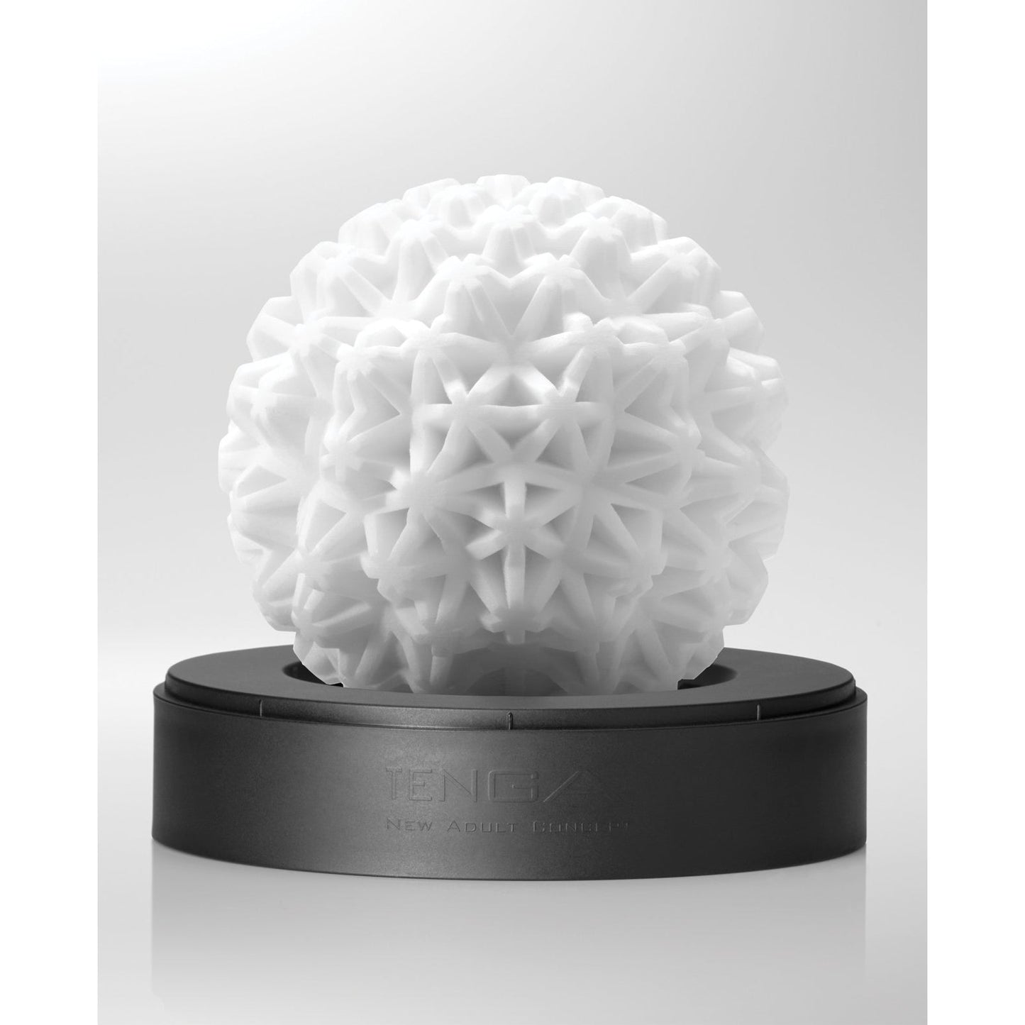The Tenga GEO Coral - White from Tenga is a reusable, spherical sculpture featuring a geometric texture. It rests elegantly on a black base against a light gray background, offering visual and sensual pleasure.