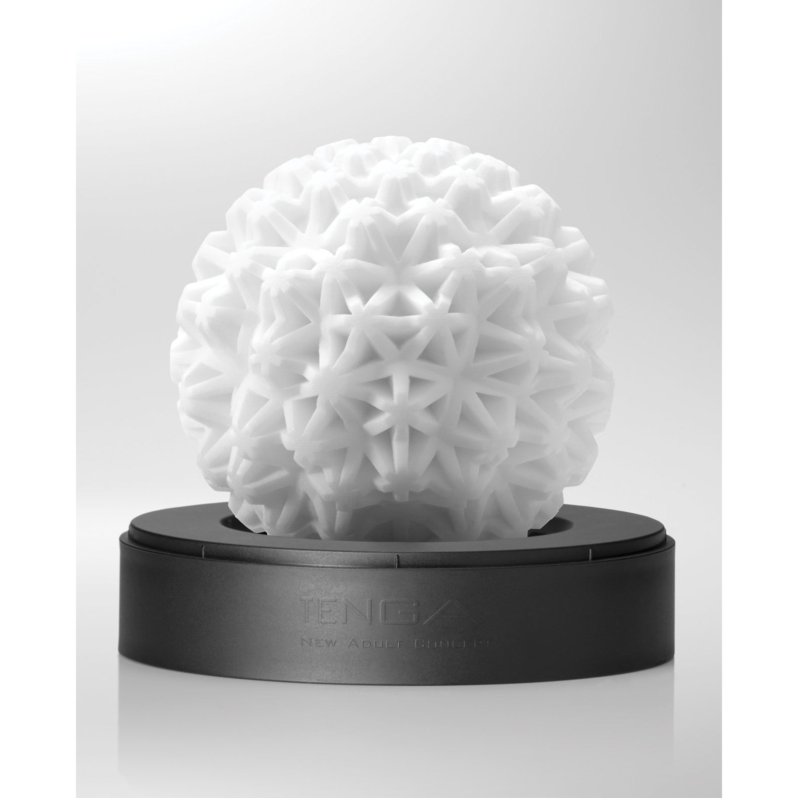 The Tenga GEO Coral - White from Tenga is a reusable, spherical sculpture featuring a geometric texture. It rests elegantly on a black base against a light gray background, offering visual and sensual pleasure.