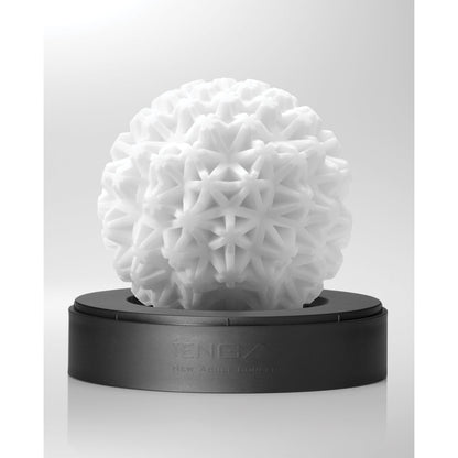 The Tenga GEO Coral - White from Tenga is a reusable, spherical sculpture featuring a geometric texture. It rests elegantly on a black base against a light gray background, offering visual and sensual pleasure.