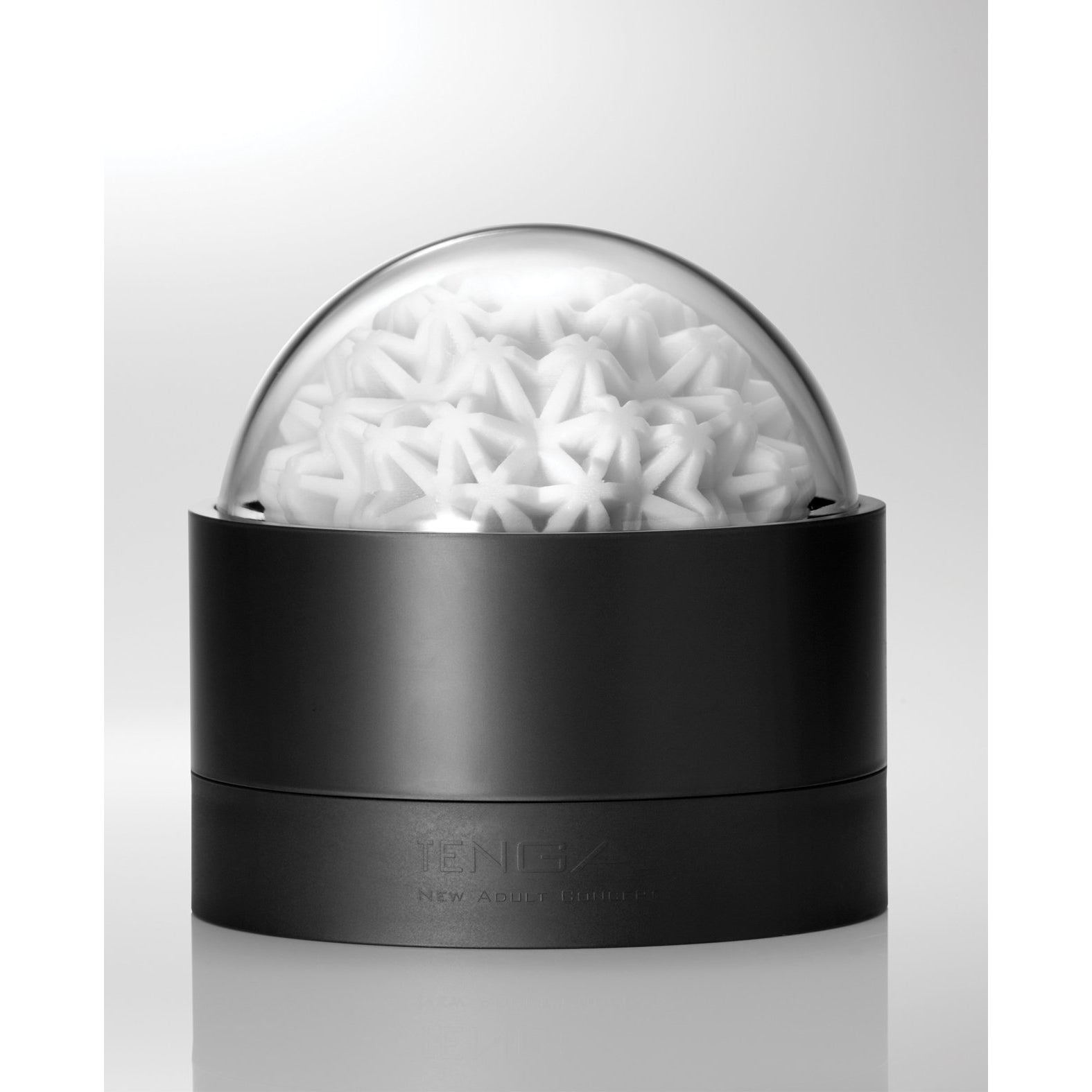 A black cylindrical container with a transparent dome lid showcases many small, white star-shaped objects. The reflective surface and soft lighting enhance its modern design. This reusable piece captures the elegant essence of the Tenga GEO Coral - White.