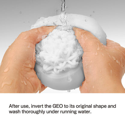 Under running water, hands squeeze a Tenga GEO Coral - White, showcasing its snowflake design. Instructions below advise: Invert the GEO to its original shape after use and wash thoroughly. This elegant Tenga product is crafted for reusable enjoyment.
