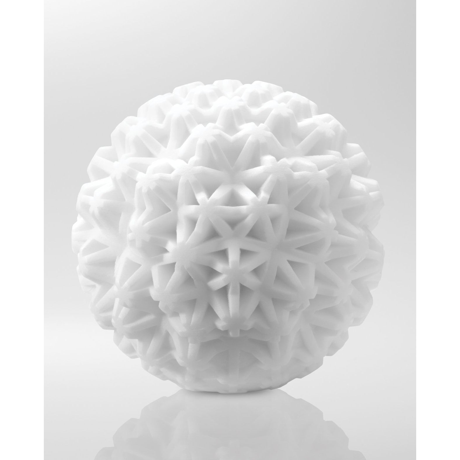 The Tenga GEO Coral - White by Tenga is a spherical sculpture featuring a complex, three-dimensional pattern of interlocking star-like shapes. This elegant piece offers reusable aesthetic appeal against any plain background, enhancing the space with its presence.