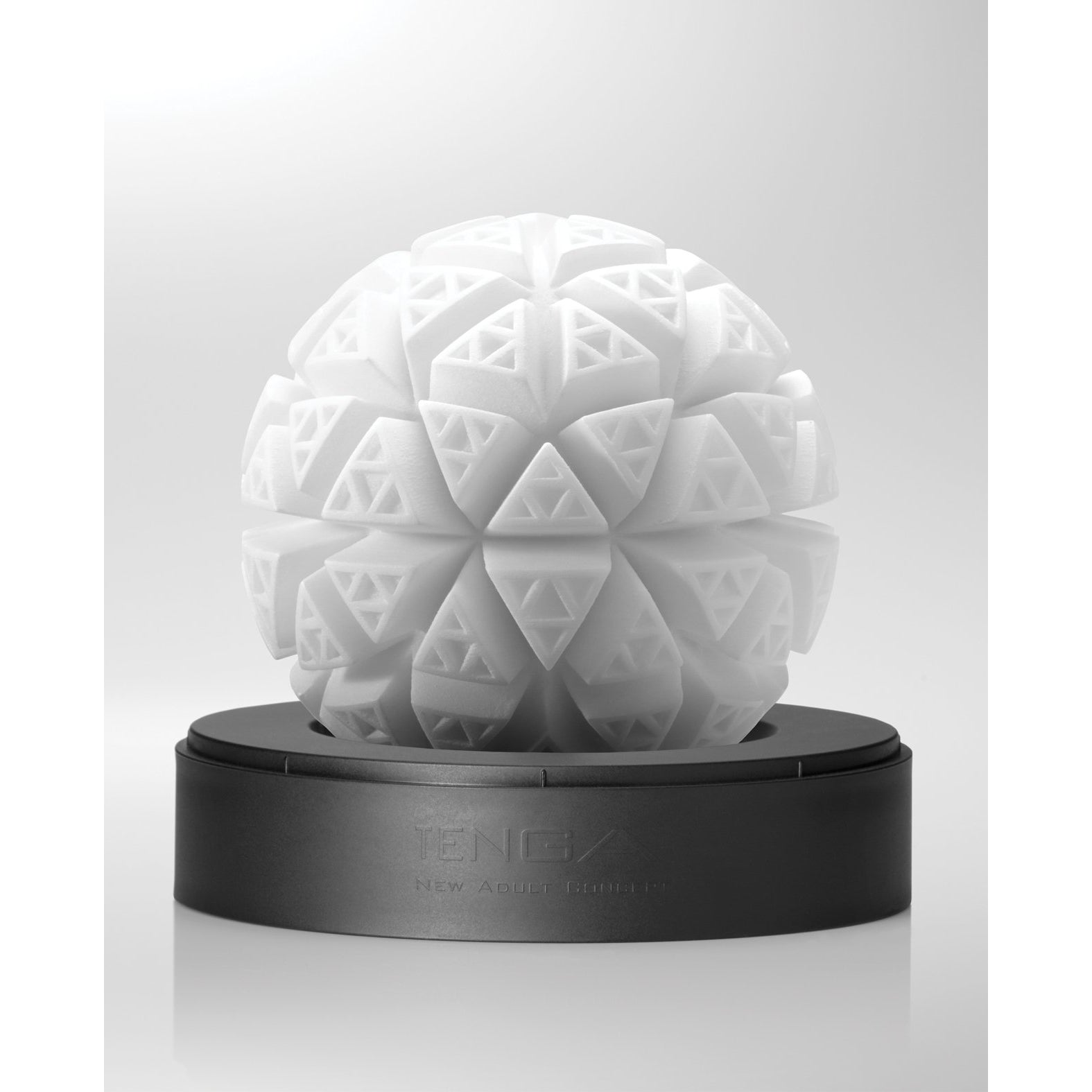 A white spherical sculpture, inspired by the Tenga GEO Glacier - White, features intricate geometric patterns on a black circular base. Triangular shapes create a textured 3D effect with stretchable material. The brand name Tenga is elegantly engraved on the base.