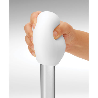 A hand grips the reusable white rounded handle of a Tenga GEO Glacier by Tenga, attached to a metal pole against a gray background.